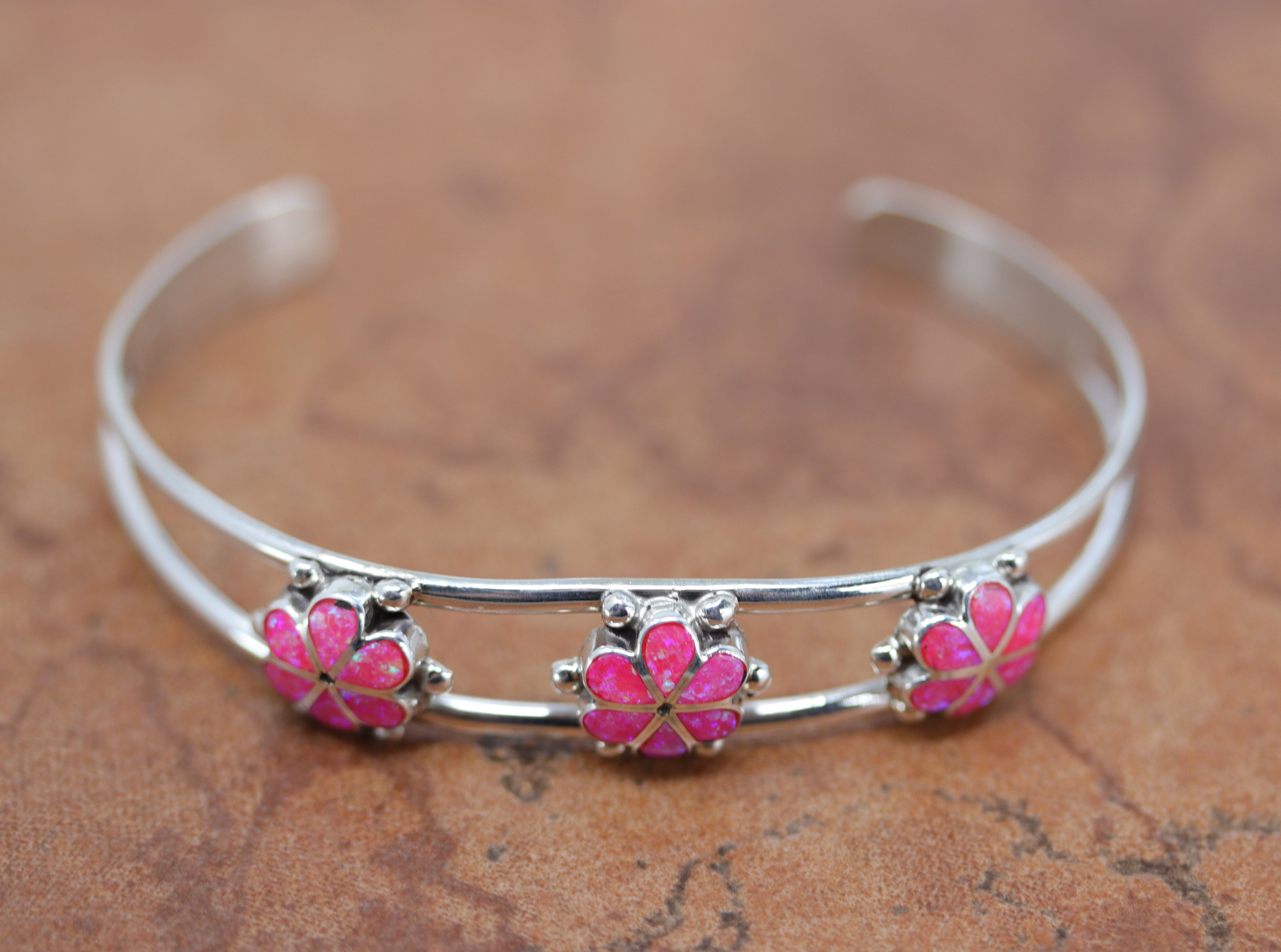 A brand new, very nice, authentic Zuni Native American flower bracelet. It is made from sterling silver and pink created opal. It is about 5 1/4" around and about 1/2" wide at the widest point. The opening is about 1 1/4" and partly flexible.&nbsp;