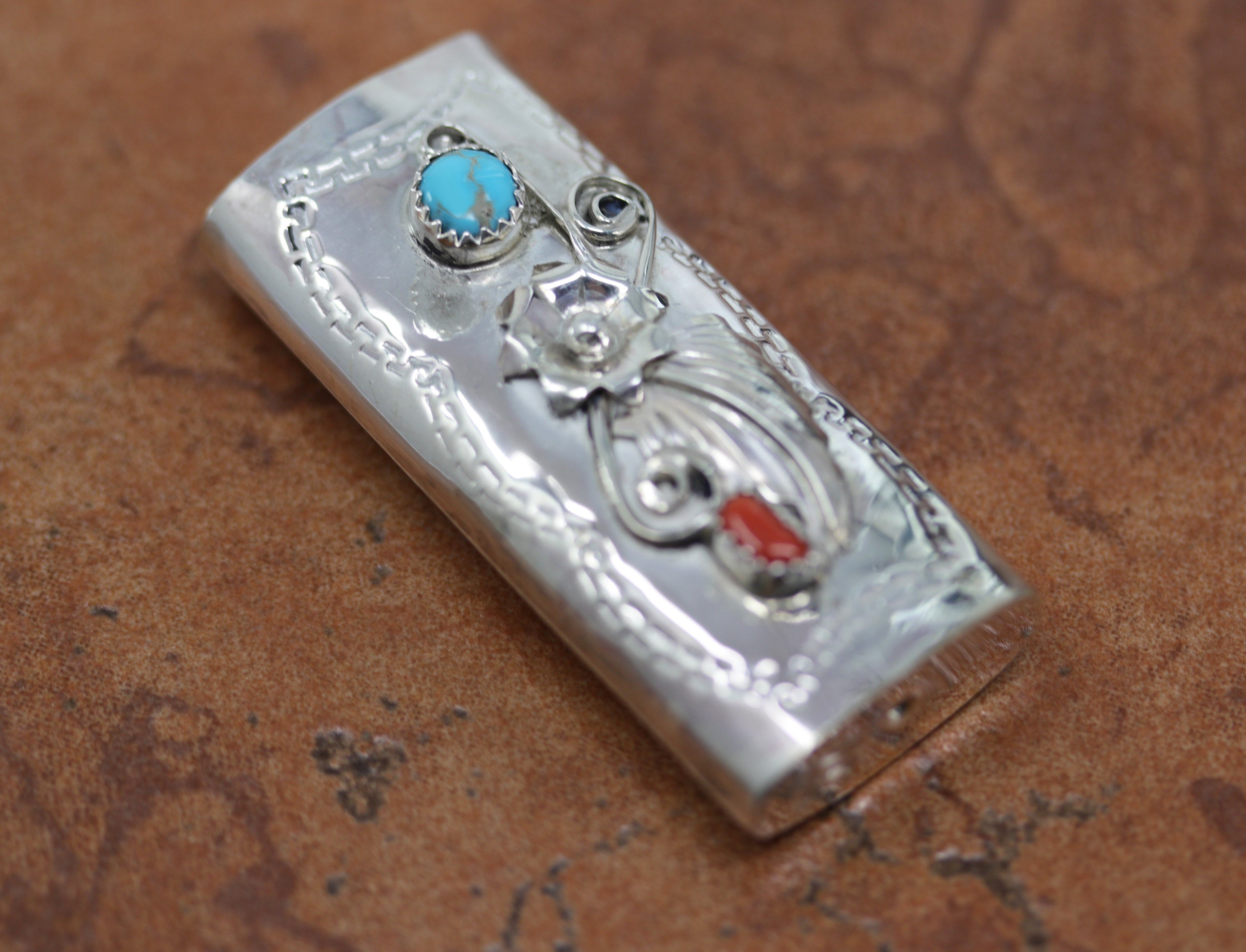 A lighter case made from sterling silver, turquoise, and coral. It measures 2 1/8" by 1".