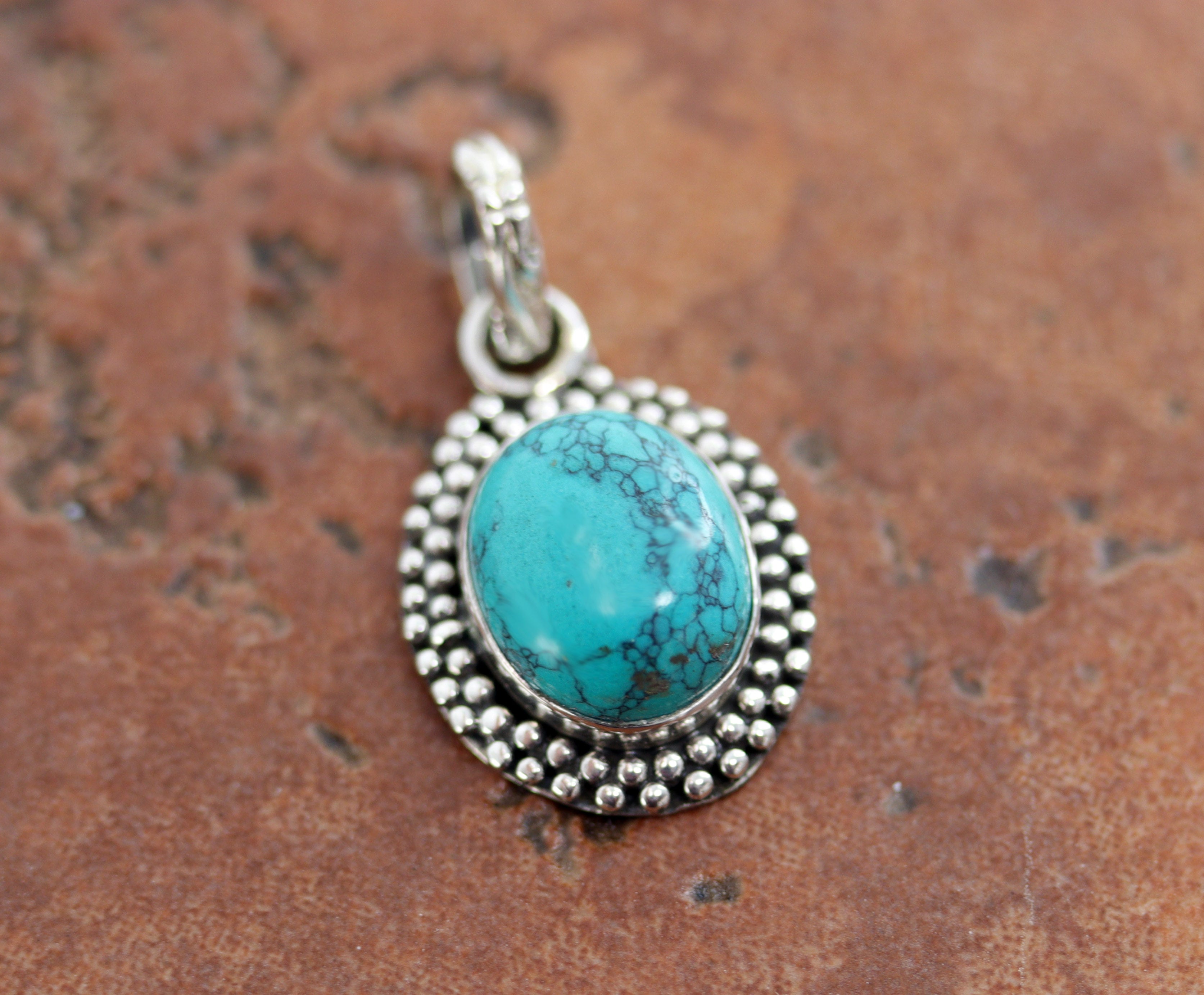 It is made from Sterling Silver and turquoise. It is about 1 5/8" in length including the bail, and about 5/8" in width. 