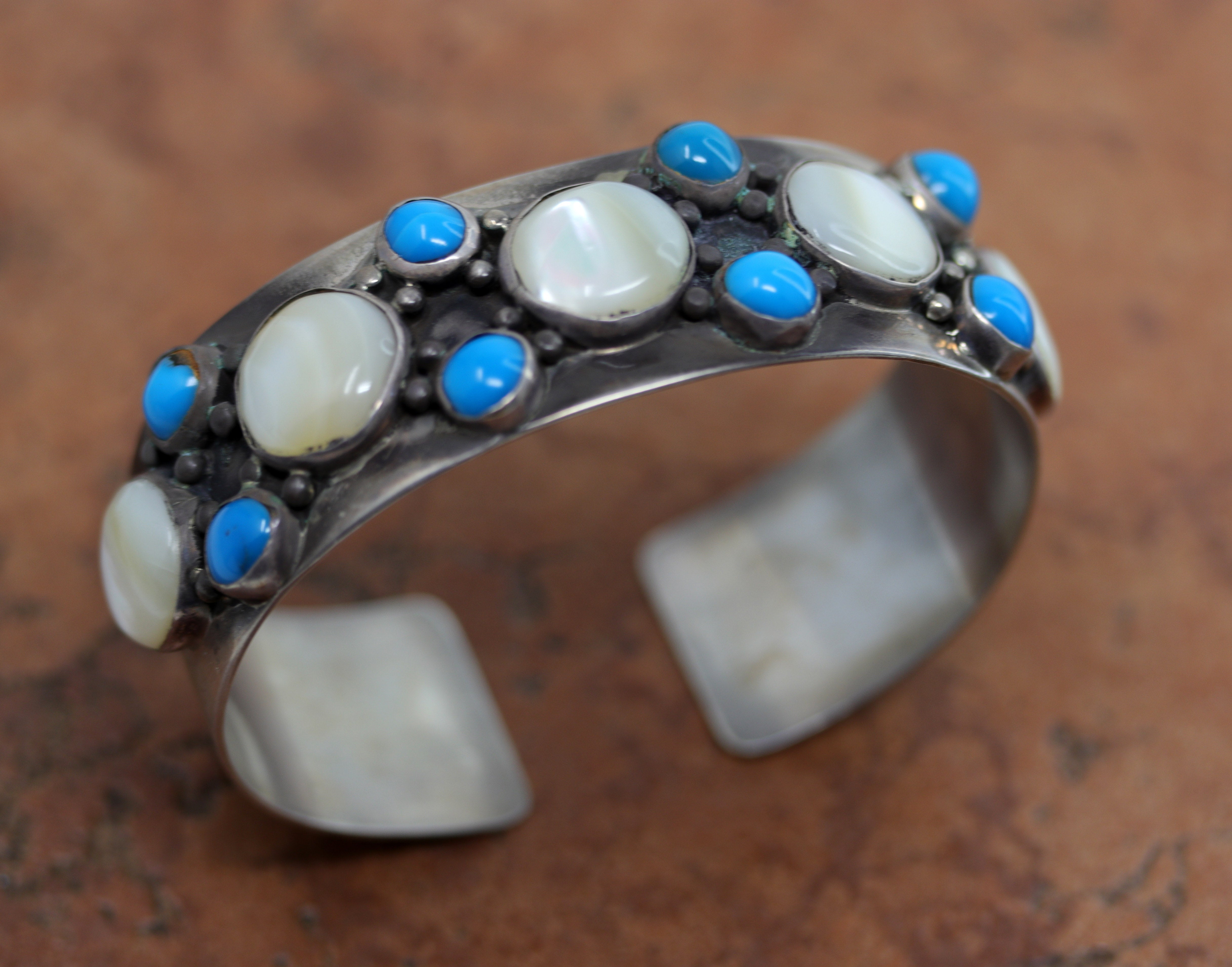 Navajo Native American bracelet by Nakai. This gorgeous cuff is made from sterling silver, mother of pearl, and turquoise. It is about 7 1/4" around and about 1 1/8" wide at the widest point. The opening is about 1", and partly flexible.