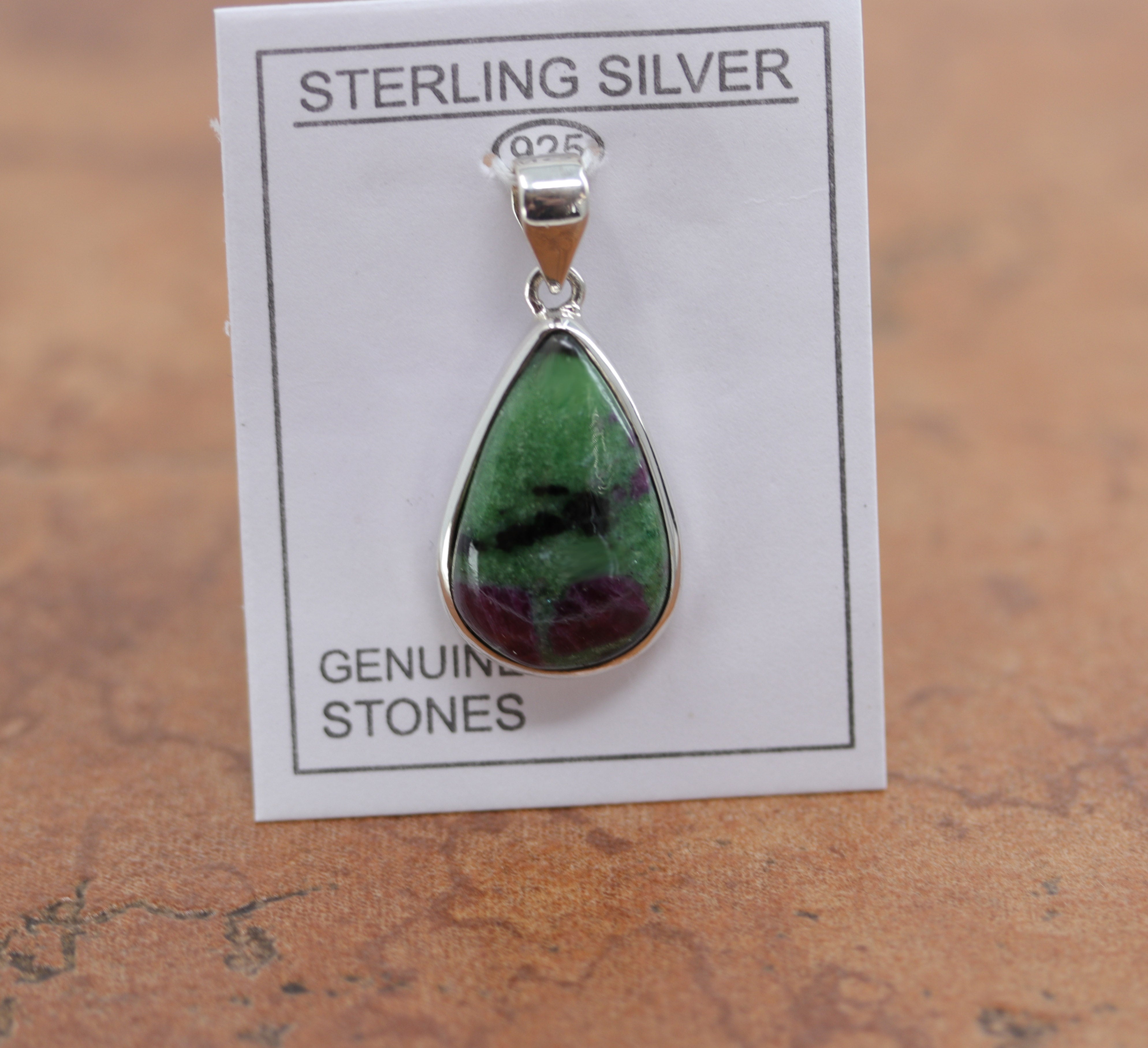 It is made from Sterling Silver and ruby zoisite. It is about 1 1/2" in length including the bail, and about 3/4" in width. 