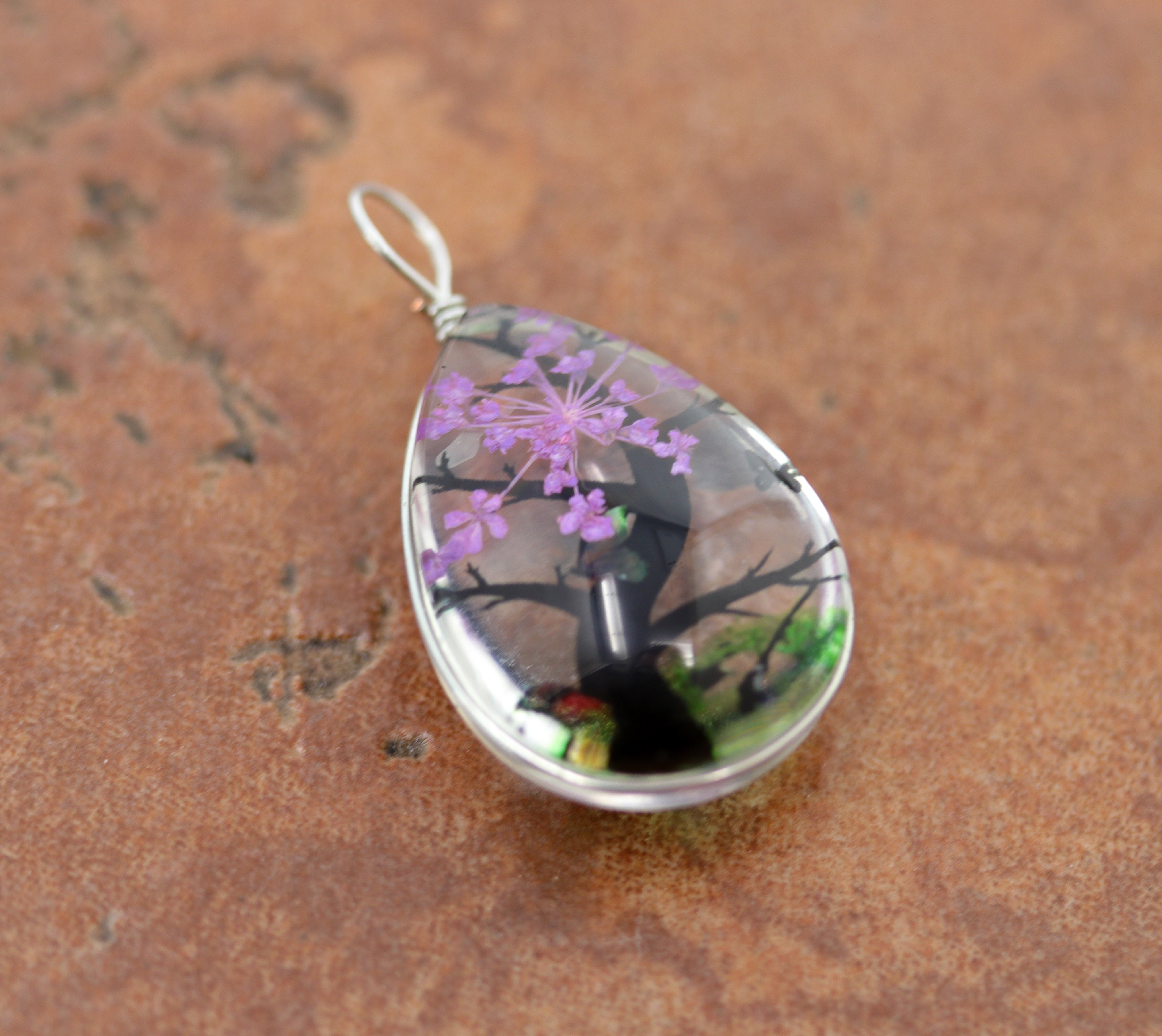 It is made from glass and purple flower petals. The pendant is about 1 3/8" in length including the bail, and about 3/4" wide.