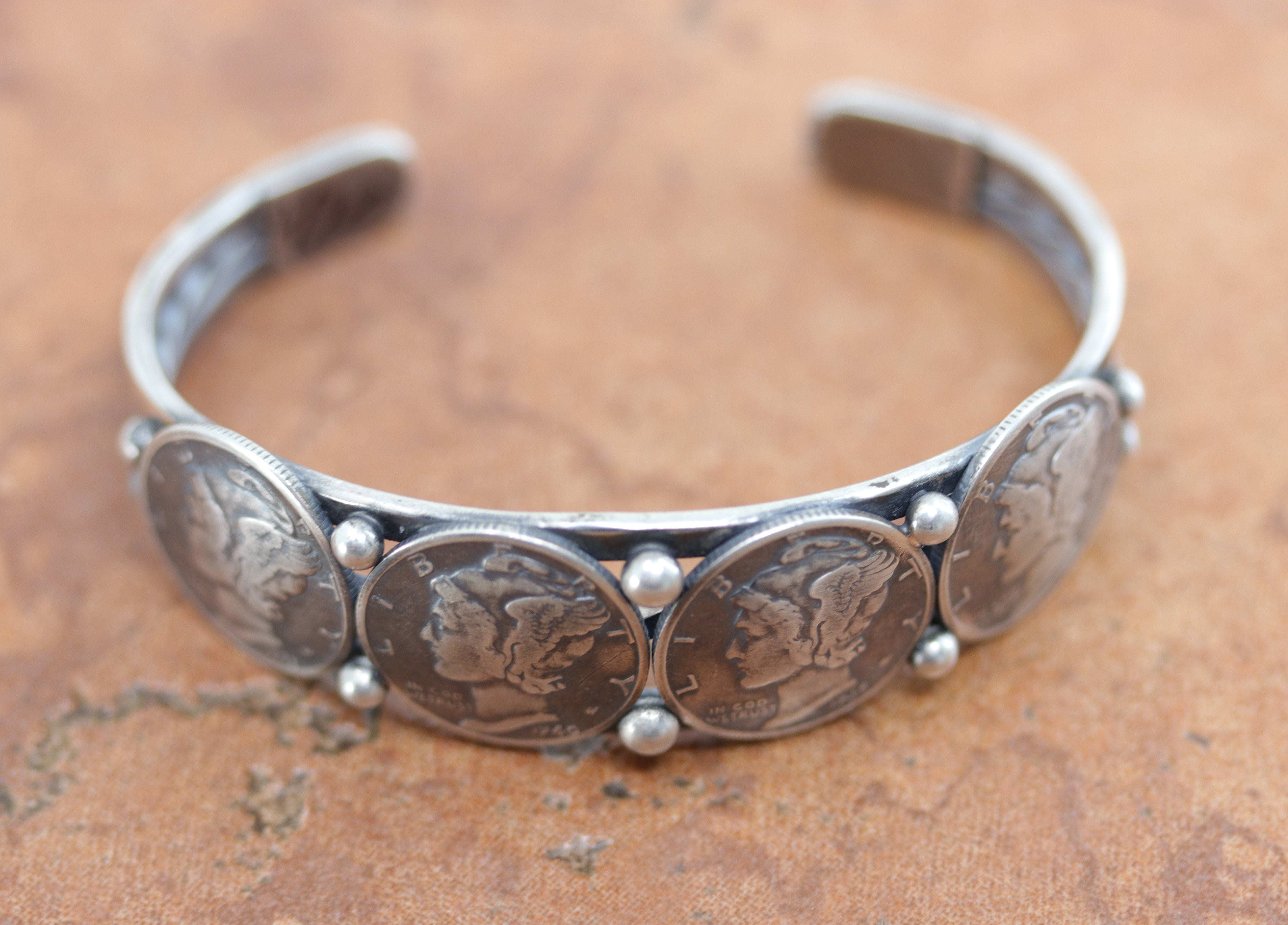 A beautiful Native American bracelet by L Archuleta. It is made from sterling silver, and real coins. It is about 5 1/4" in length, not including the opening, and it is about 3/4" wide. The opening is 1" and partly flexible.