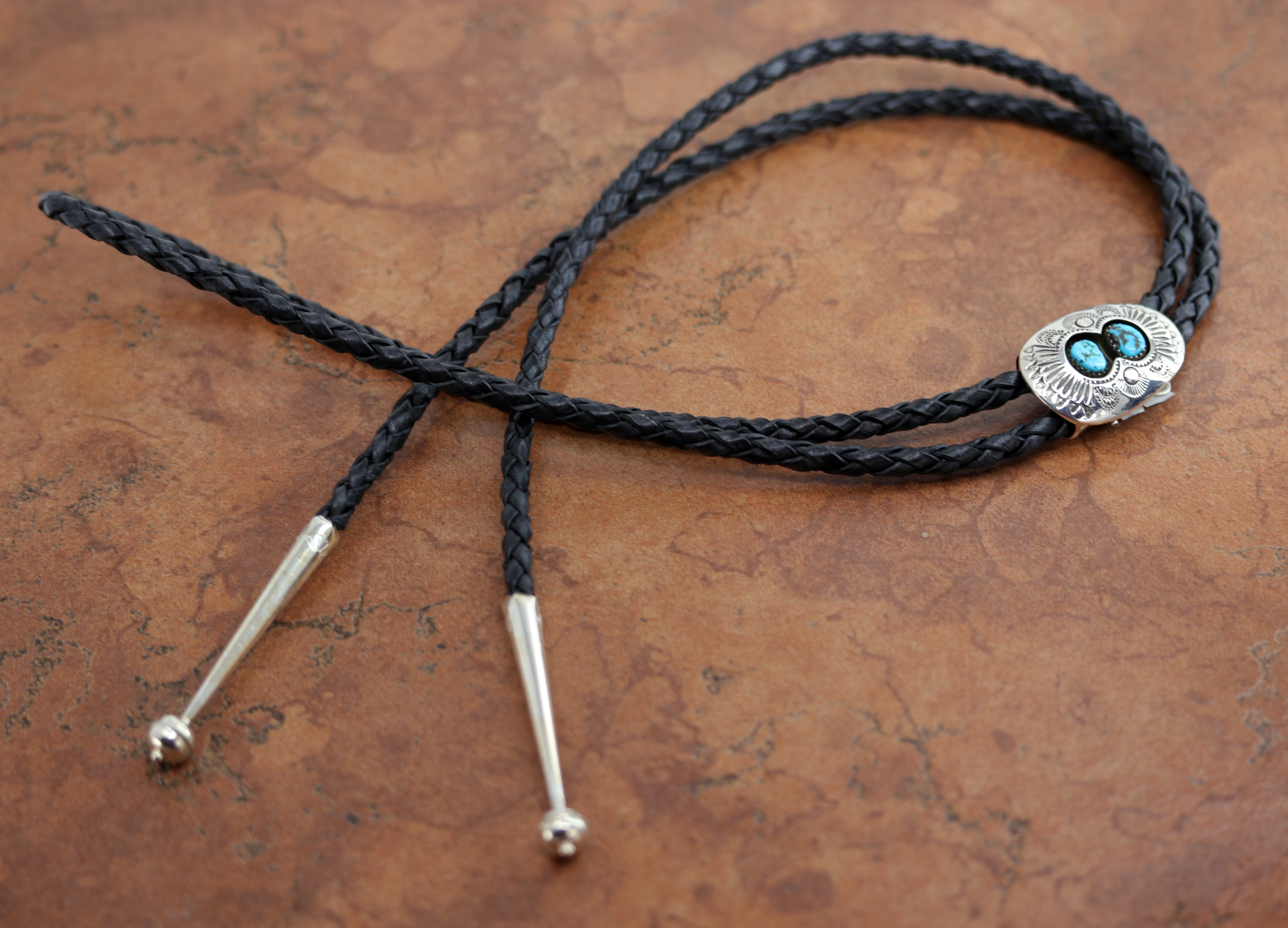 An authentic Navajo Native American Bolo Tie. The bolo tie is made of sterling silver and turquoise. The cord measures about 44". The bolo measures 1 1/2" by 1".