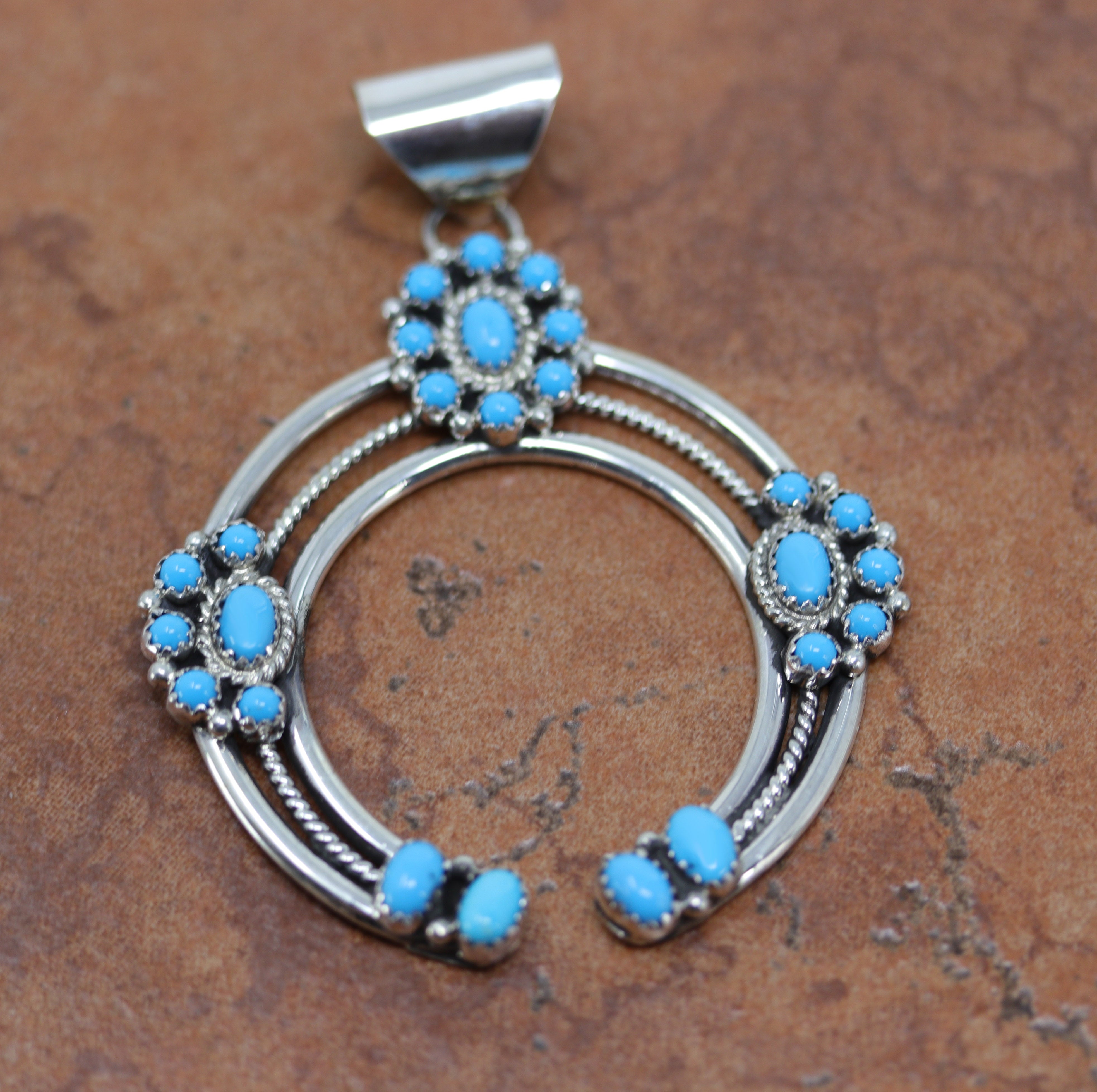 A beautiful Navajo Native American Pendant. It is made from sterling silver and turquoise. The clusters are placed on top of the naja. It is 2 7/8" long and about 2 1/8" wide.