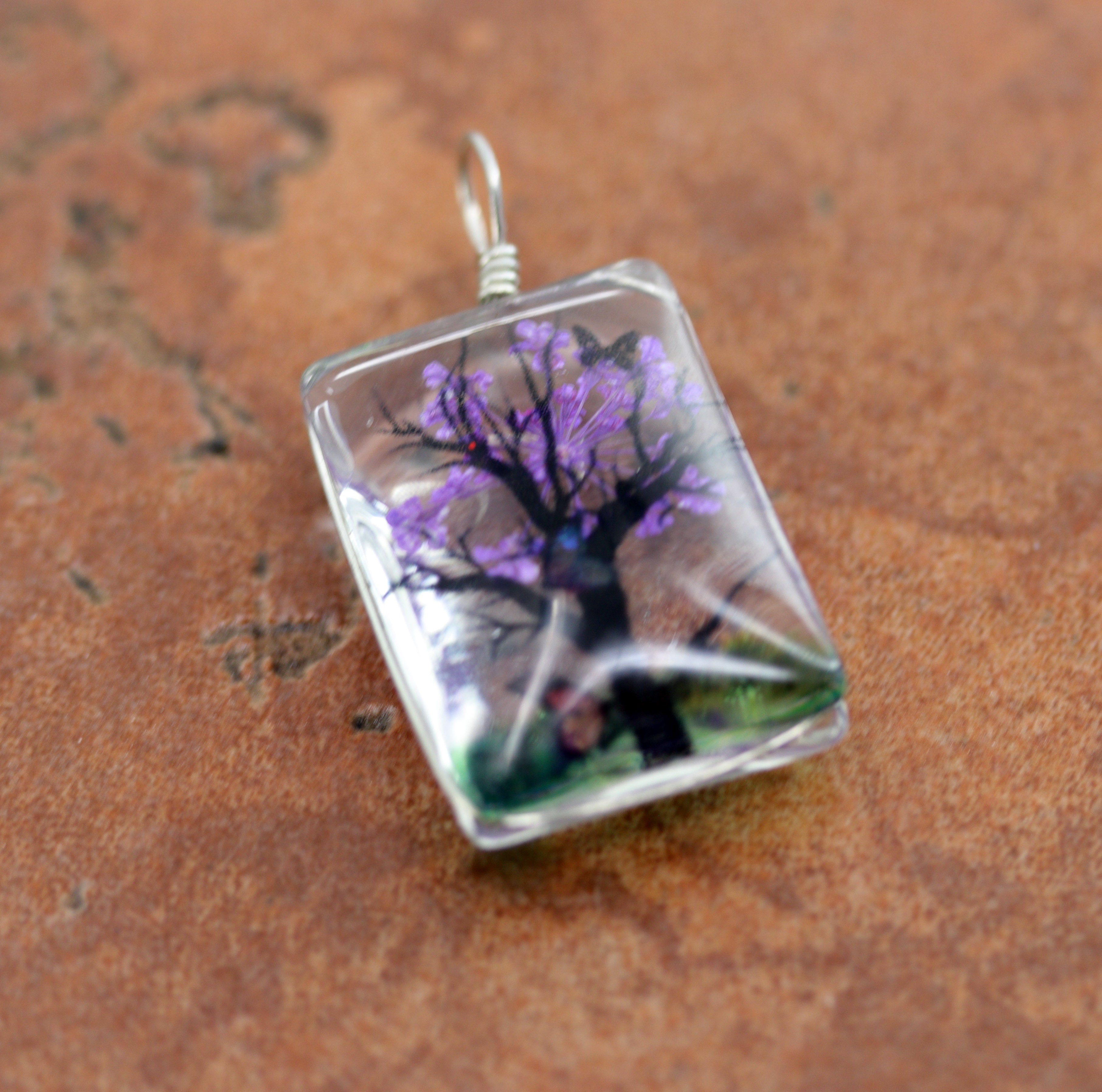 It is made from glass and purple flower petals. The pendant is about 1 3/8" in length including the bail, and about 3/4" wide.