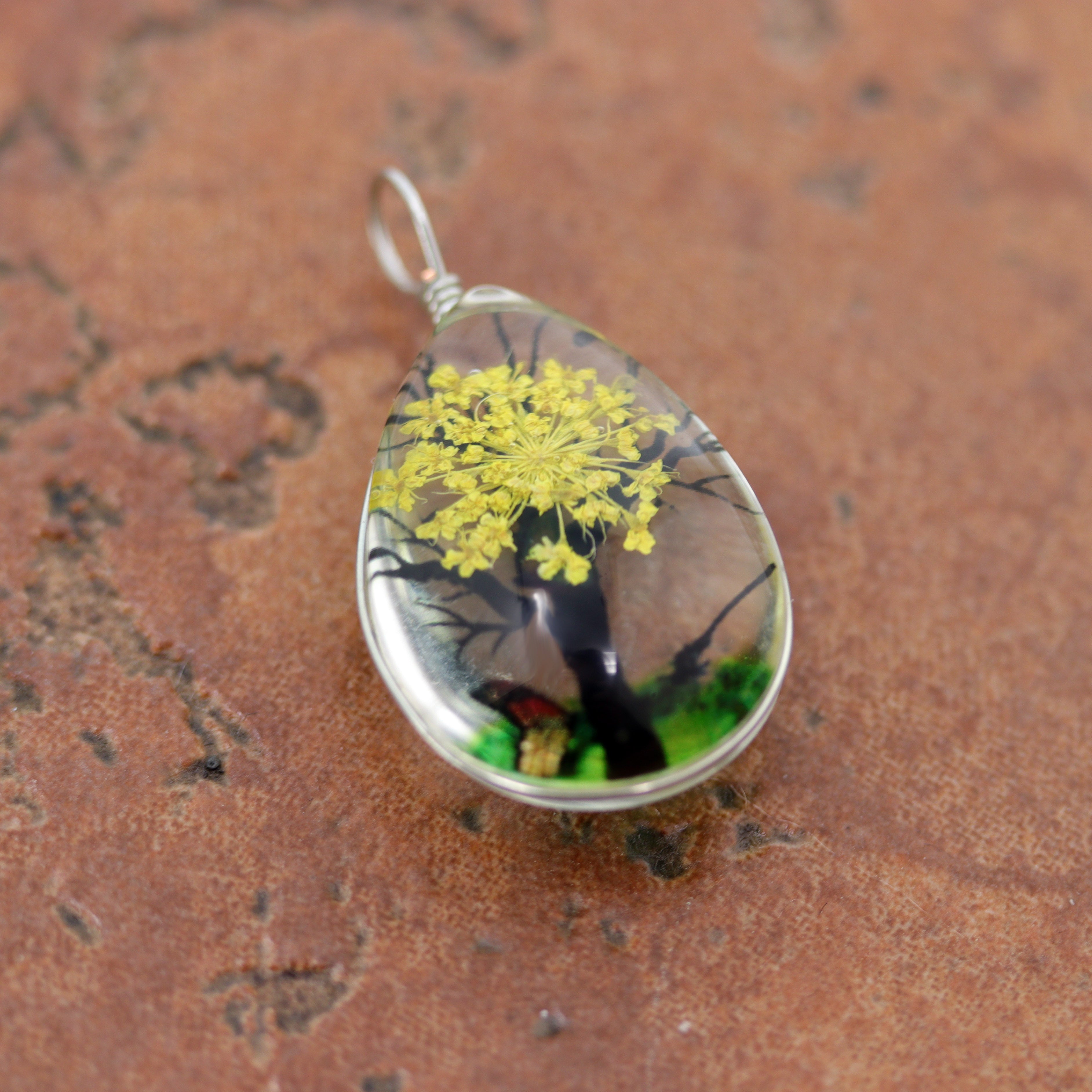 It is made from glass and yellow flower petals. The pendant is about 1 3/8" in length including the bail, and about 3/4" wide.