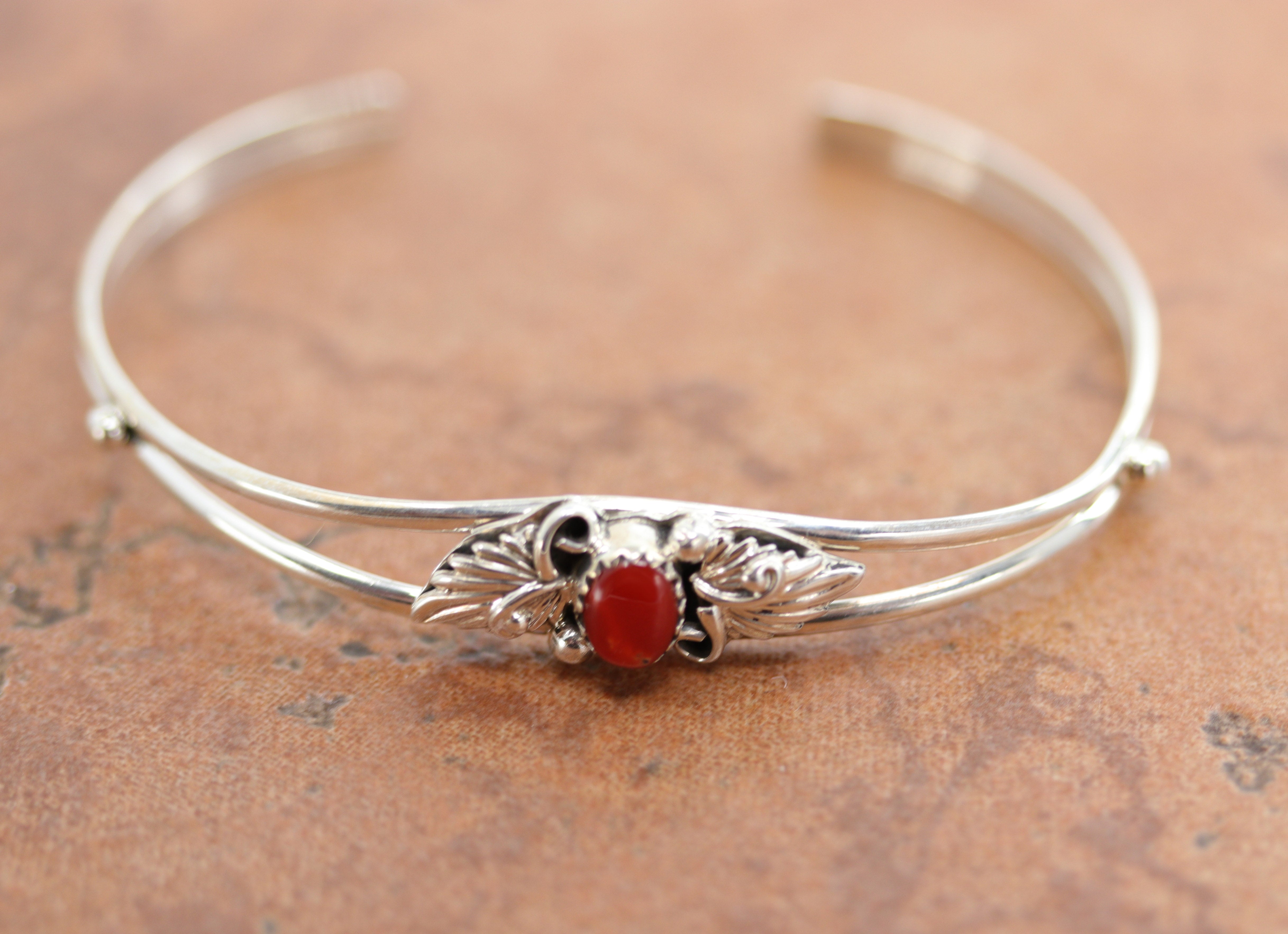 Navajo Native American bracelet. It is made from sterling silver and coral. It is about 5 1/2" around and 1/2" wide. The opening is about 1 1/2", and it is partly flexible.