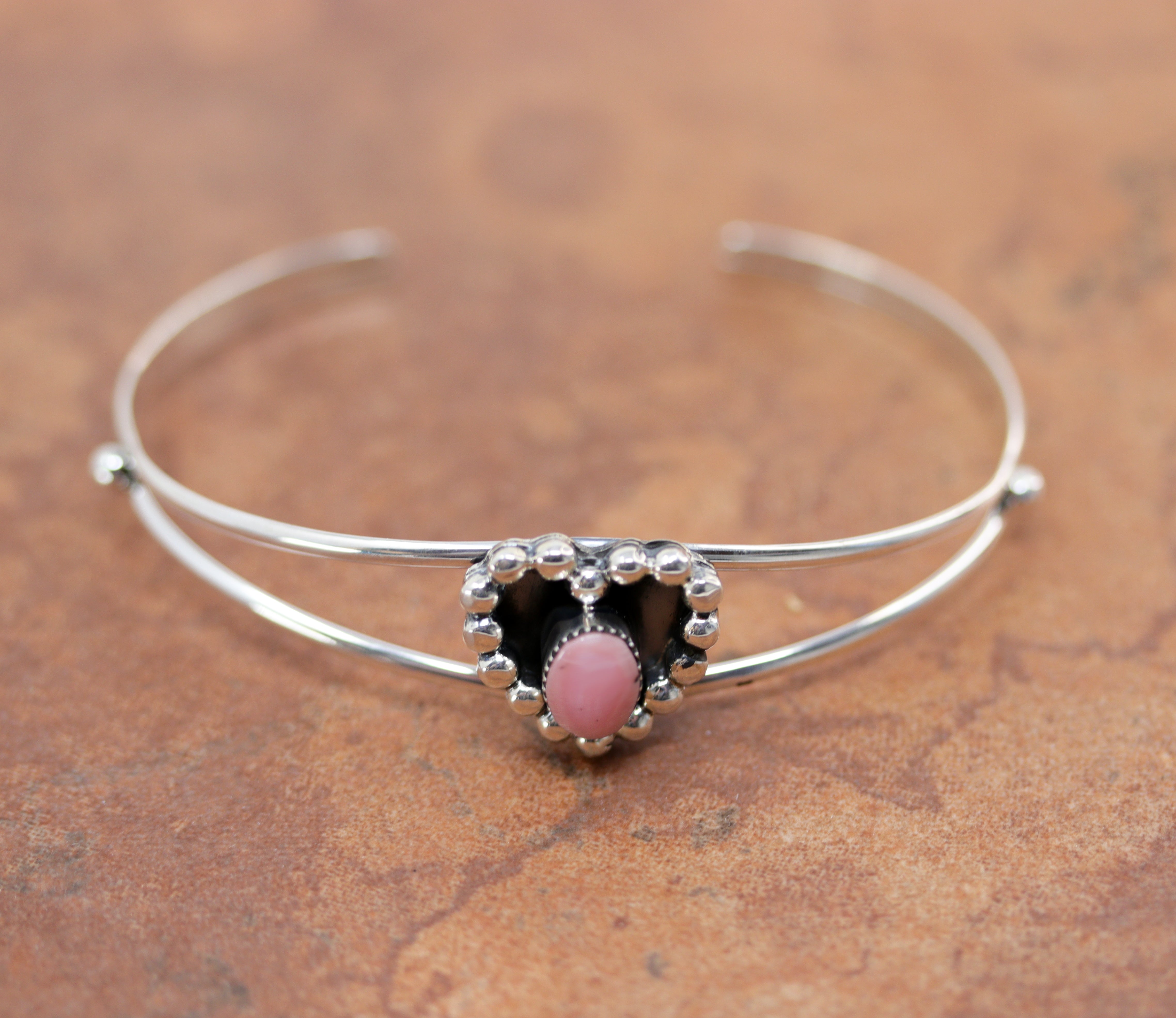 Silver bracelet with a heart shaped center and a round pink stone 