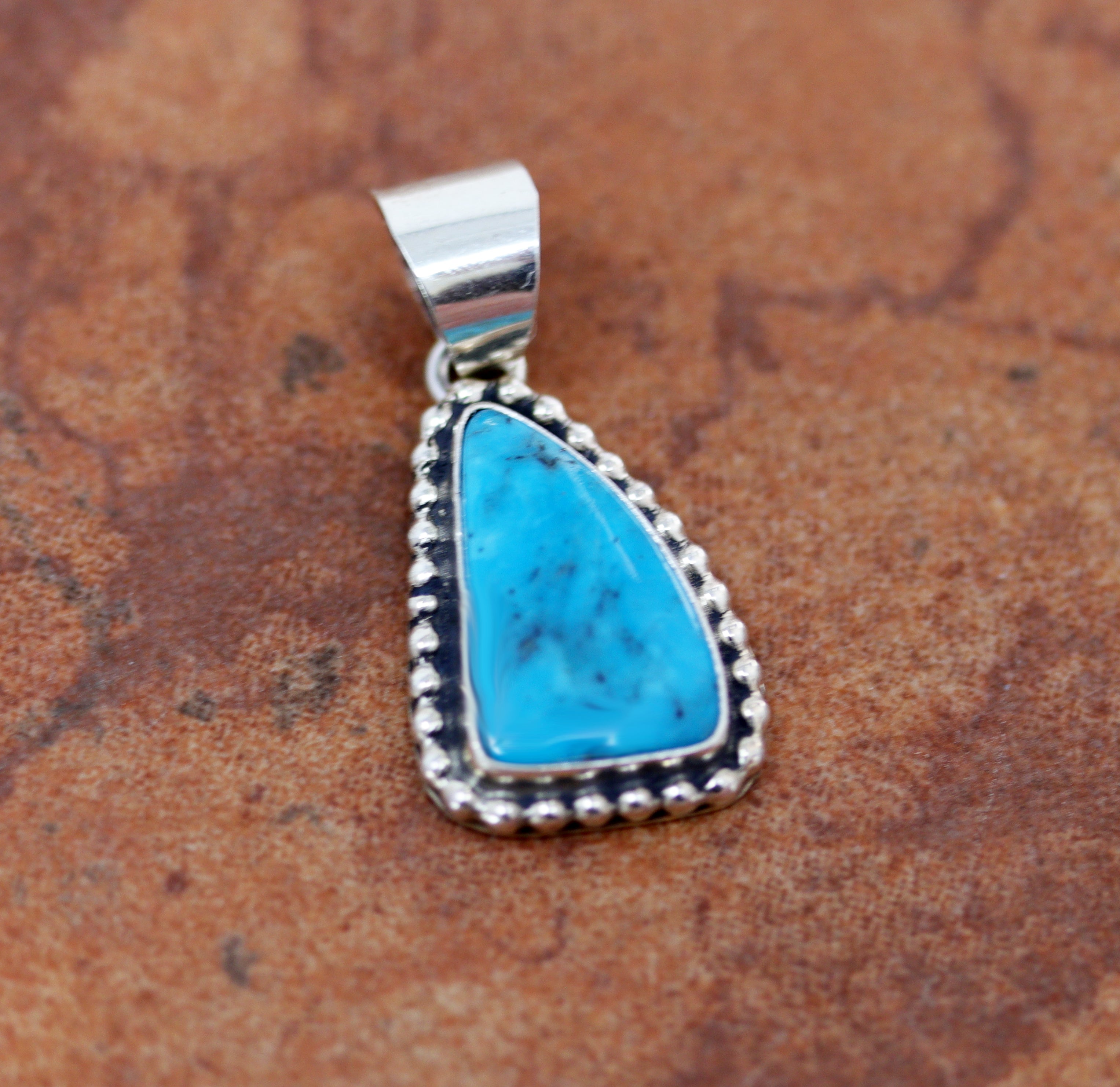 Silver pendant with a traiangular turquoise gemstone in the middle